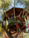 Treehouse nestled in an olive tree with colorful streamers hanging from the branches against a blue sky