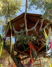 Wooden treehouse nestled in trees, decorated with colorful ribbons hanging from branches.