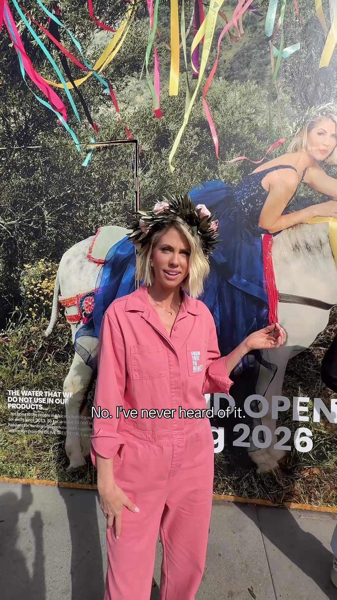 Woman in pink jumpsuit with flower-and-leaf crown in front of billboard; overlaid text reads No. I've never heard of it