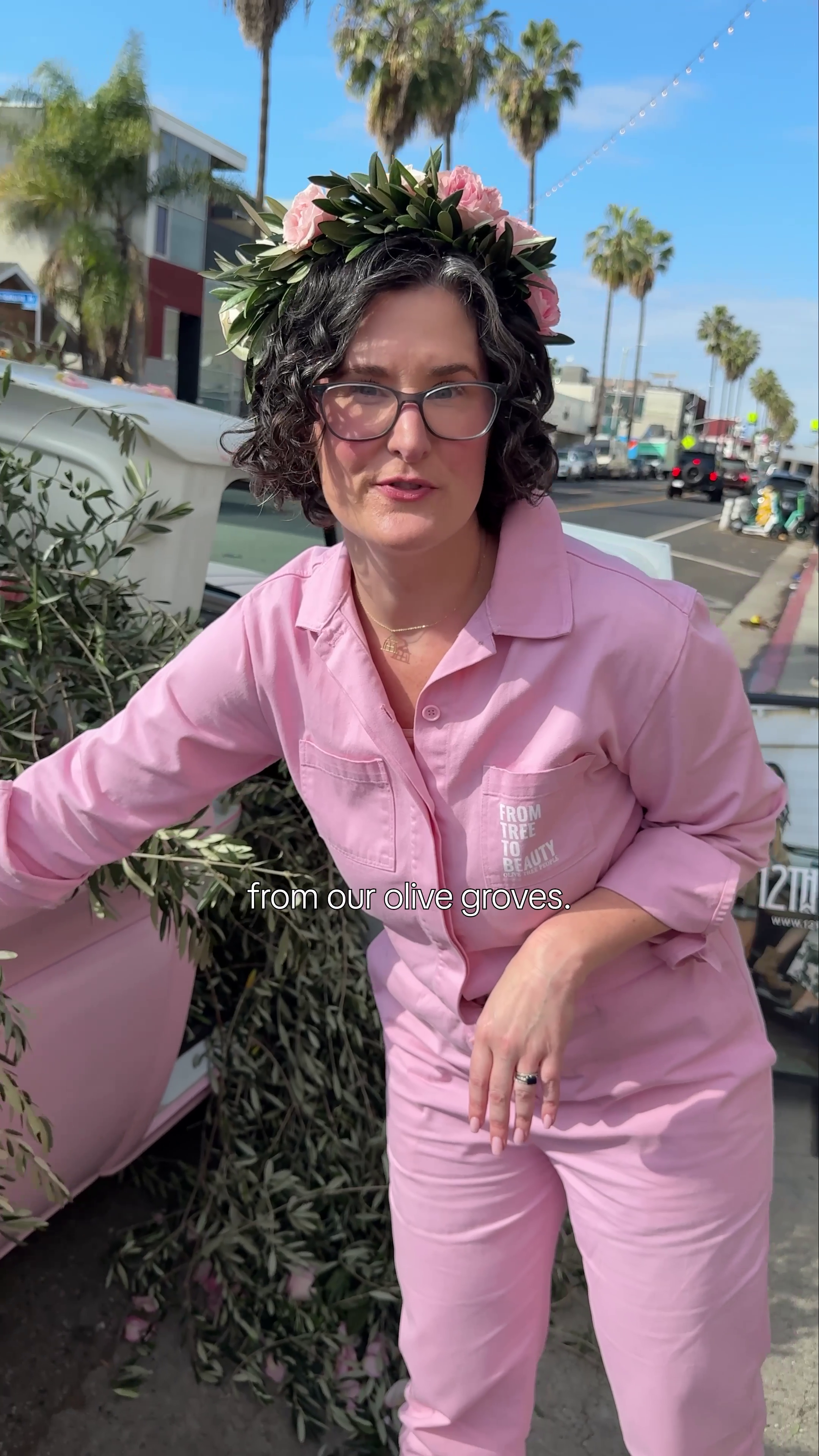 Woman in pink coveralls and flower crown next to olive branches; reads 'from our olive groves', 'FROM TREE TO BEAUTY', '12TH'