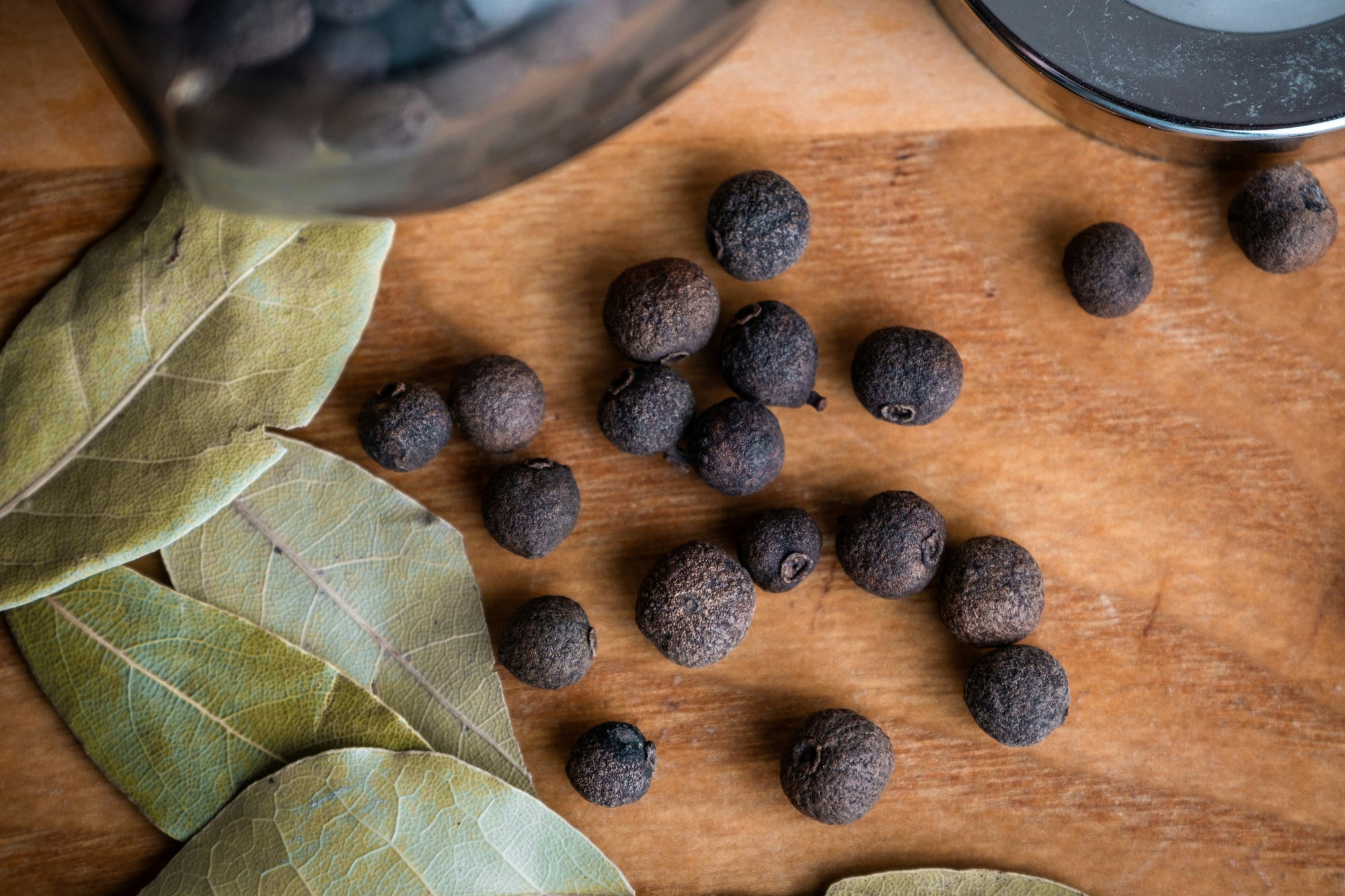 Bay leaves and whole allspice berries on a wooden cutting board