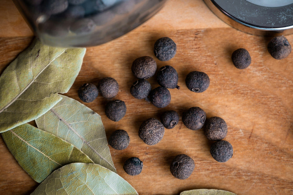 Bay leaves and whole allspice berries on a wooden cutting board