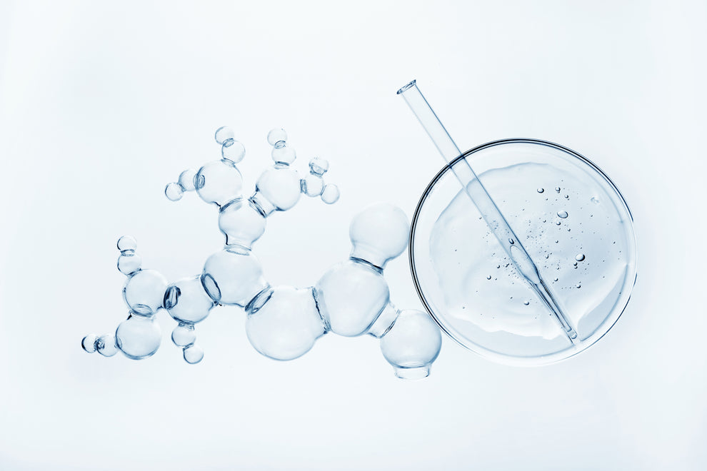 Glass molecular model made of joined clear spheres beside a petri dish and pipette with clear liquid and droplets.