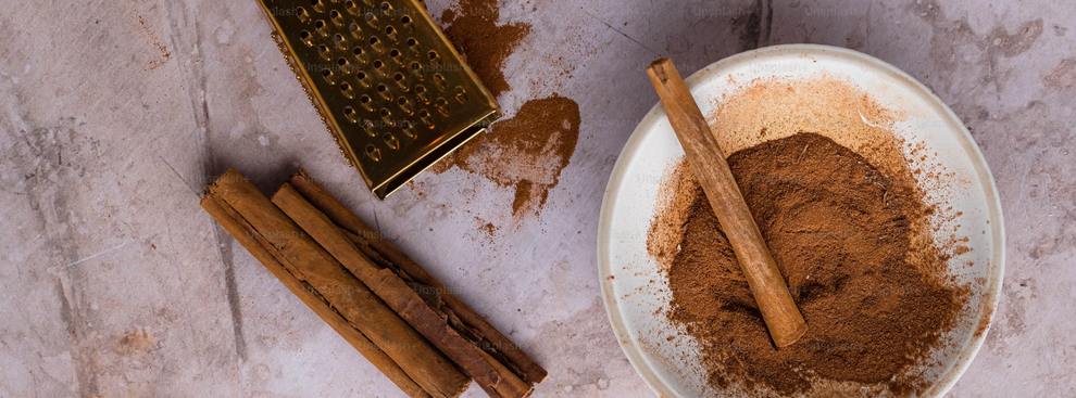 Cinnamon sticks and ground cinnamon on a plate with a grater; 'Unsplash' watermark visible