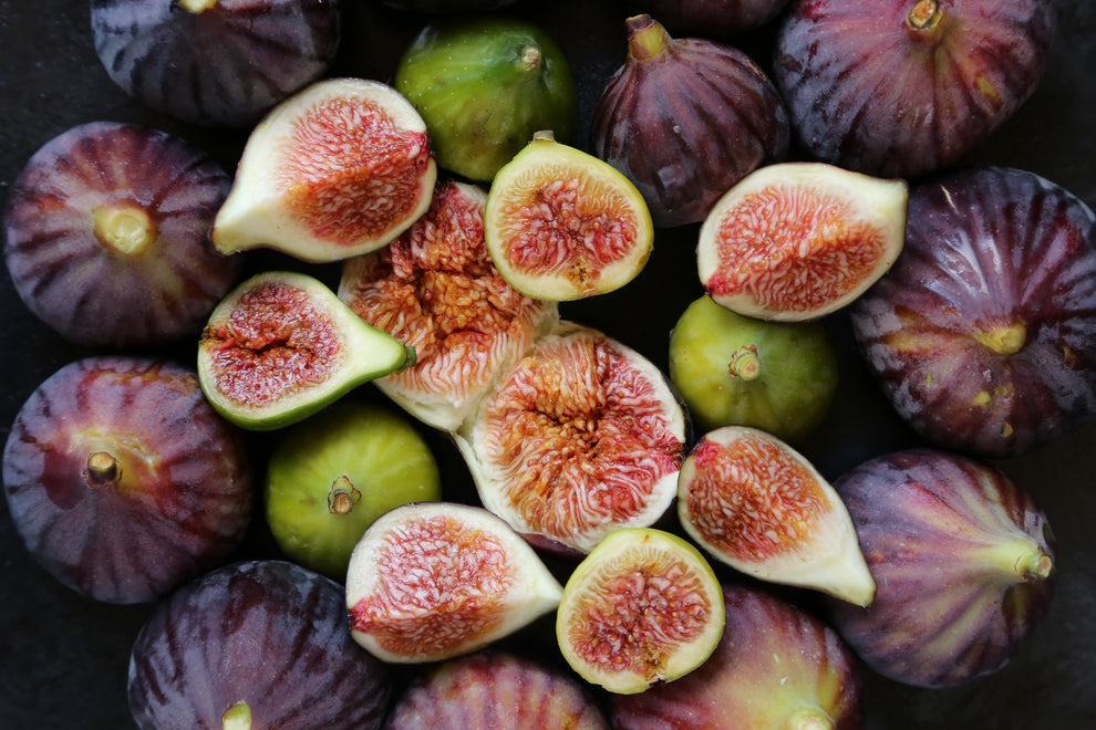 Assorted ripe figs, whole and halved, showing red-seeded interiors on a dark surface