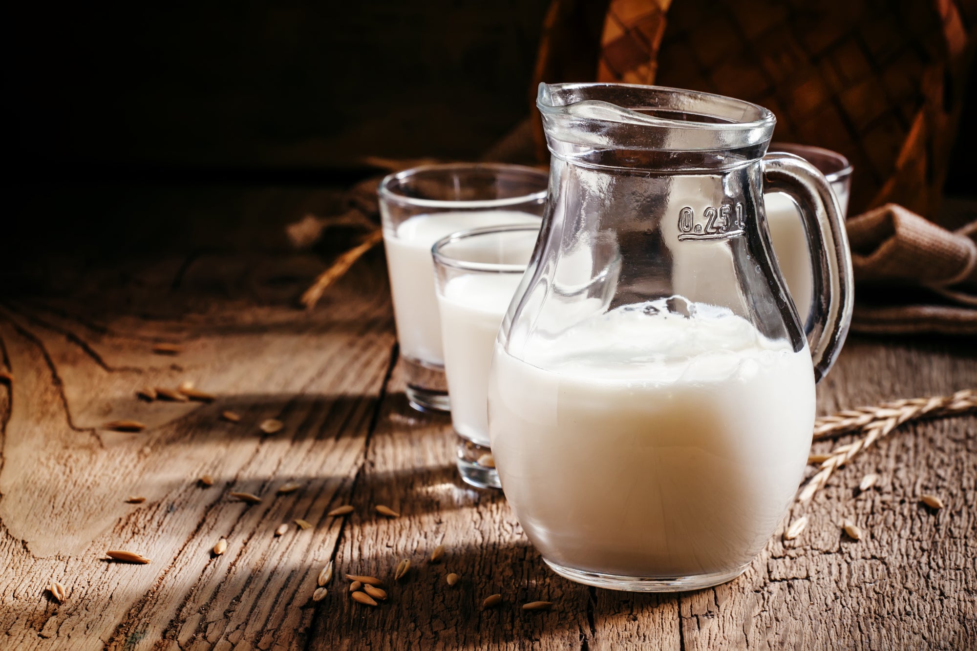 Glass pitcher of milk marked 0.25 l, with two filled glasses behind on a rustic wooden table