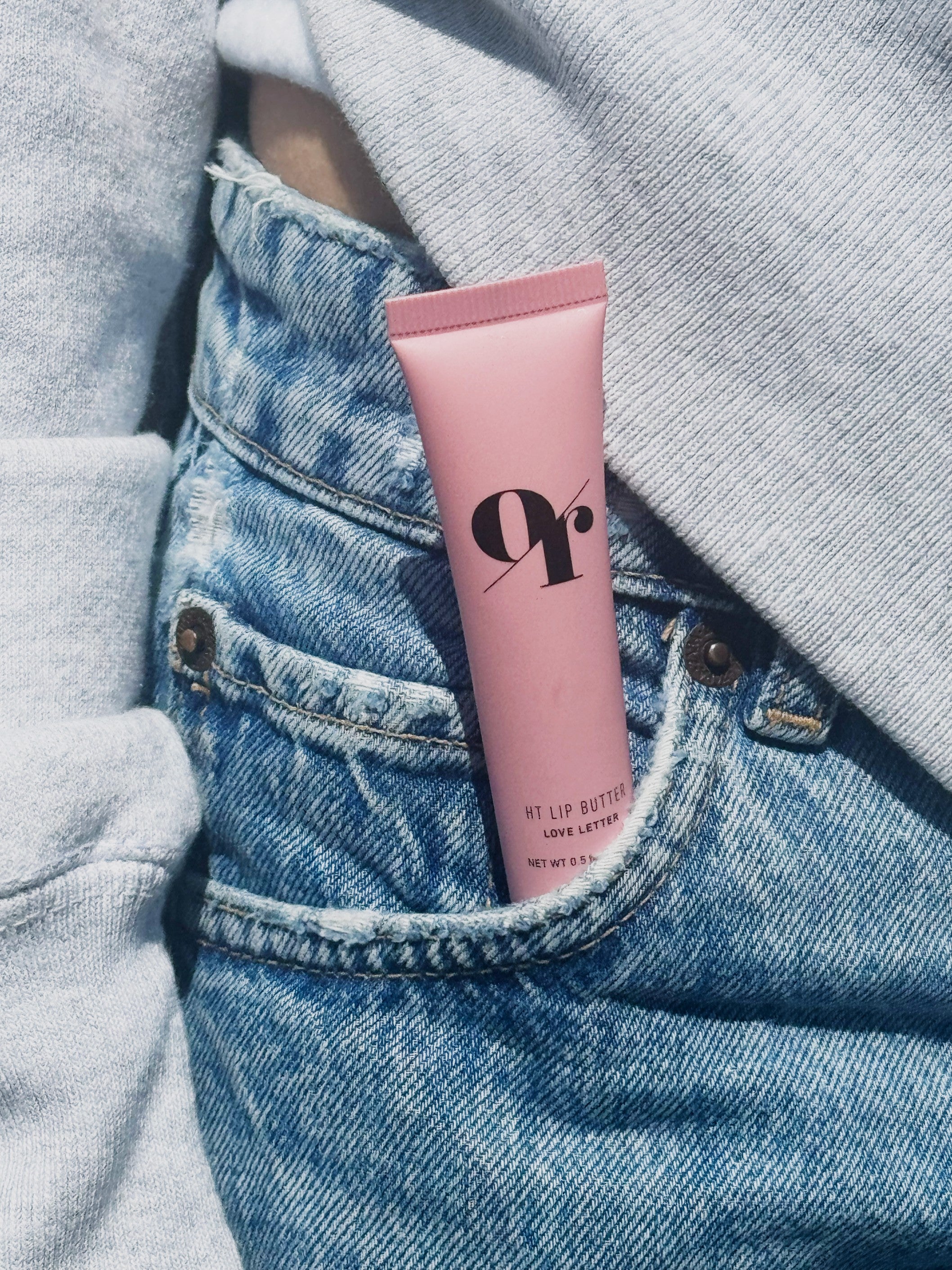 Pink lip butter tube labeled 9r, HT LIP BUTTER LOVE LETTER NET WT 0.5, tucked into a blue denim front pocket