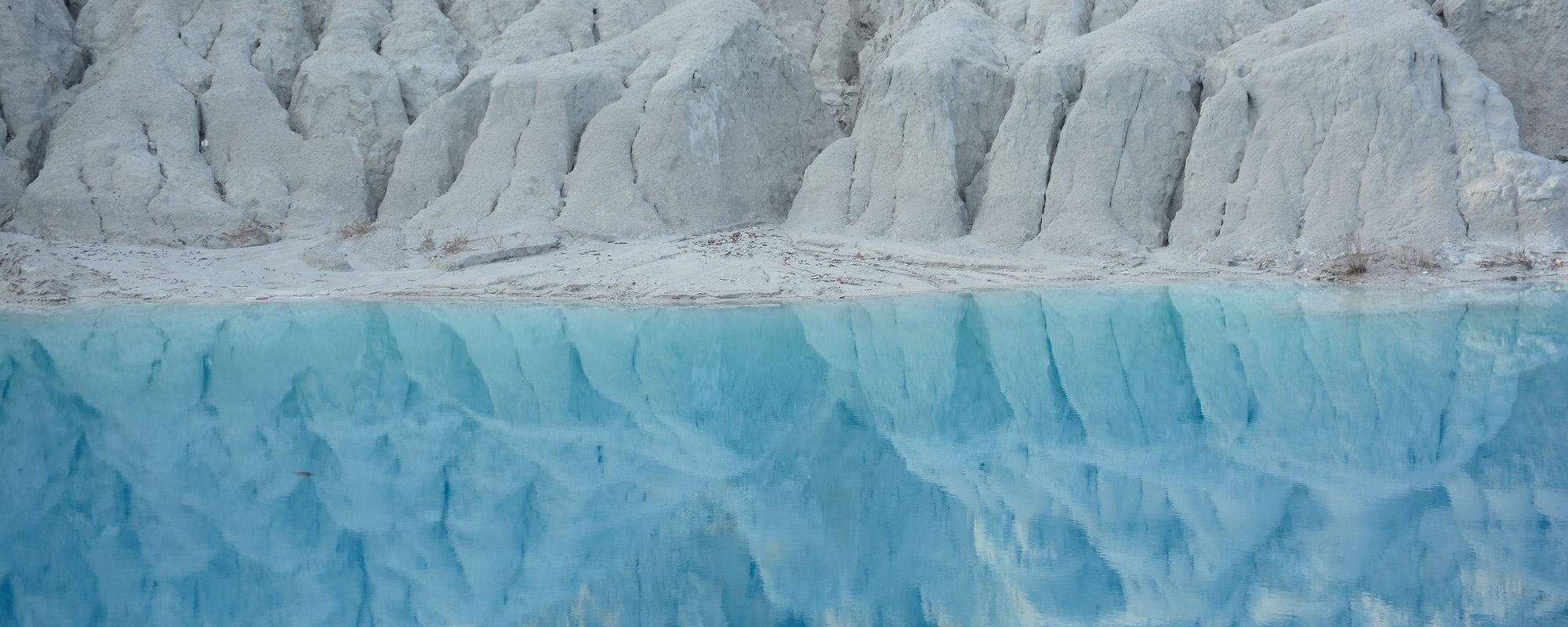 Pale eroded cliffs reflected in clear turquoise lake