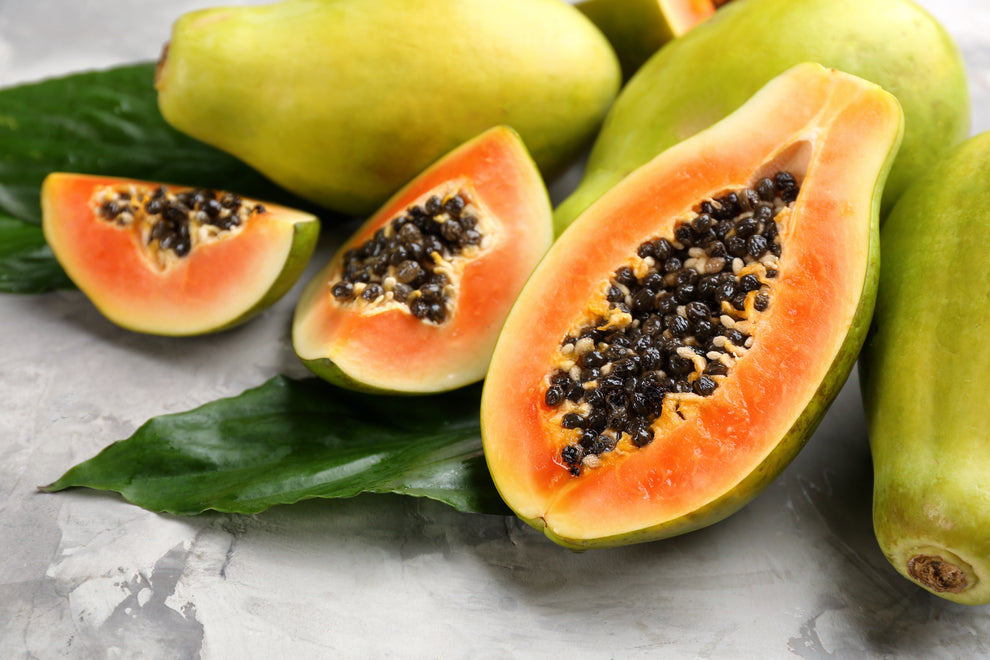 Halved ripe papayas with orange flesh and black seeds resting on green leaves