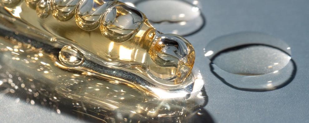 Close-up of golden viscous serum droplets and smear on a blue-gray surface with light reflections.