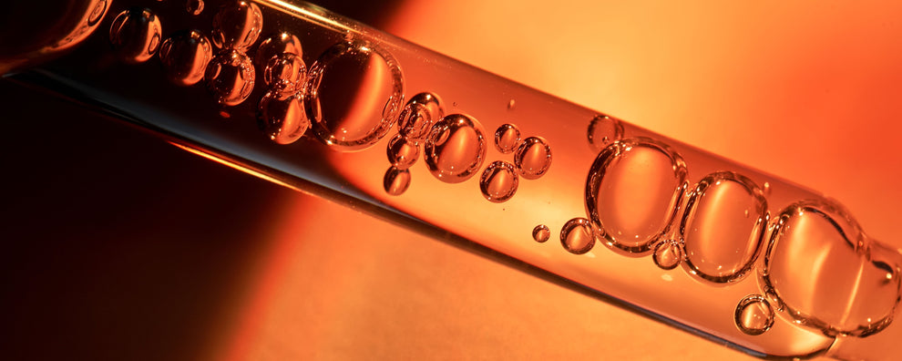 Close-up of bubbles suspended in orange-tinted liquid inside a glass test tube.