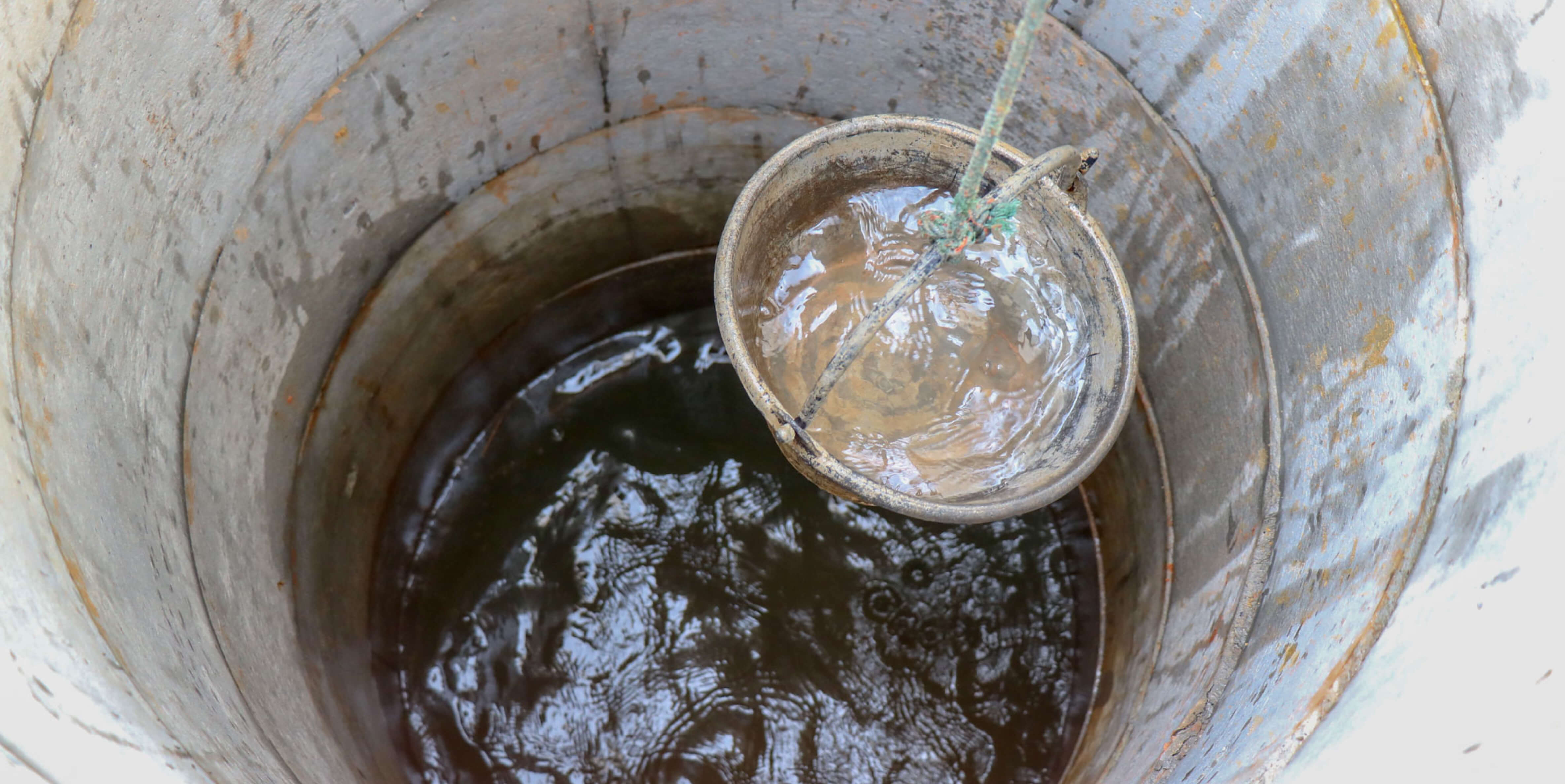 Metal bucket on a rope scooping murky water from a concrete well